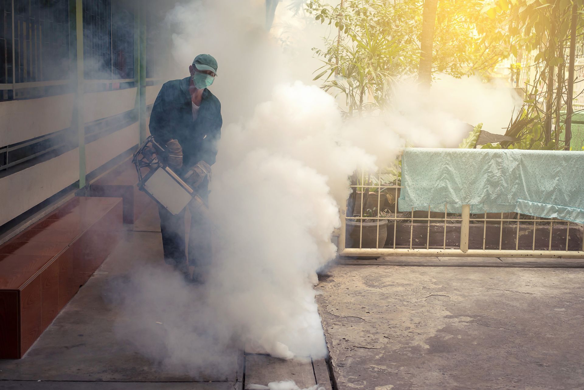 Pest control technician fogging the outside of a building with a handheld fogger