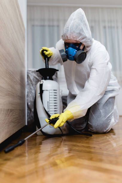 Pest control technician in a protective suit and respirator treating a room with a sprayer